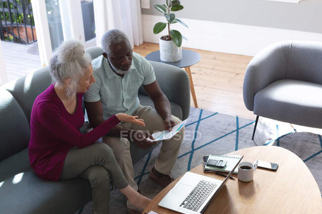 Senioren-Mischlingspaar mit Laptop im Wohnzimmer beim Bezahlen von Rechnungen. Während der Quarantäne zu Hause bleiben und sich selbst isolieren. — Stockfoto