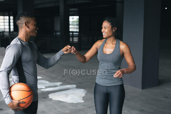 Un homme et une femme afro-américains debout dans un bâtiment urbain vide et le poing cognant. forme physique urbaine mode de vie sain. — Photo de stock