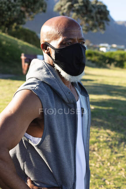 Homem americano africano sénior a usar máscara facial a exercitar-se ao ar livre. aposentadoria saudável fitness ao ar livre estilo de vida higiene durante coronavírus covid 19 pandemia. — Fotografia de Stock