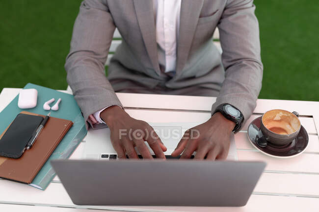 Homem de negócios afro-americano sentado em um café usando laptop e bebendo café. homem de negócios em movimento na cidade. — Fotografia de Stock