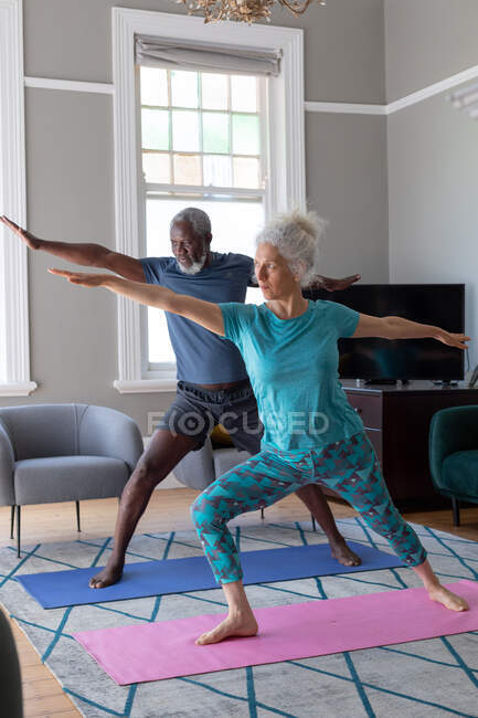 Coppia di anziani misti che indossa vestiti sportivi che si esercitano in soggiorno. stare a casa in isolamento durante l'isolamento in quarantena. — Foto stock