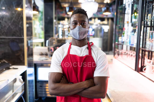 Porträt eines afrikanisch-amerikanischen Baristas mit Gesichtsmaske, der in die Kamera blickt. Gesundheit und Hygiene in Unternehmen während der Coronavirus-Pandemie 19. — Stockfoto