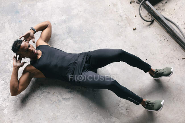 Homme afro-américain portant des vêtements de sport faisant des craquements dans un bâtiment urbain vide. forme physique urbaine mode de vie sain. — Photo de stock