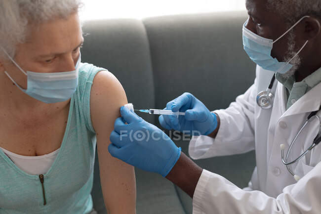 Doctor wearing surgical gloves giving senior female woman covid 19 vaccination at home. healthcare and hygiene at home in self isolation during quarantine lockdown. — Stock Photo
