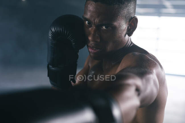 African american man wearing boxing gloves throwing punches in air in empty building. urban fitness healthy lifestyle. — Stock Photo