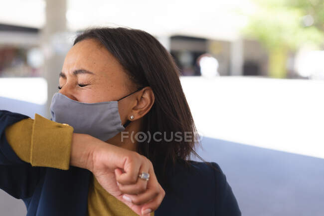 Африканская американка в маске для лица чихает на руку на улице. образ жизни во время пандемии коронавируса 19. — стоковое фото