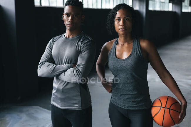 Un homme et une femme afro-américains debout dans un bâtiment urbain vide regardant une caméra. forme physique urbaine mode de vie sain. — Photo de stock