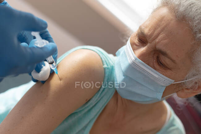 Medico indossando guanti chirurgici dando anziana donna covid 19 vaccinazione a casa. — Foto stock