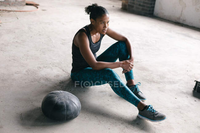 Afroamerikanerin sitzt an einem Medizinball in einem leeren städtischen Gebäude. urbane Fitness gesunder Lebensstil. — Stockfoto