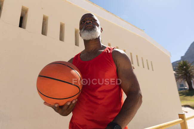 Ajuste hombre afroamericano mayor de pie en el sol celebración de baloncesto. deporte de jubilación saludable estilo de vida fitness al aire libre. - foto de stock