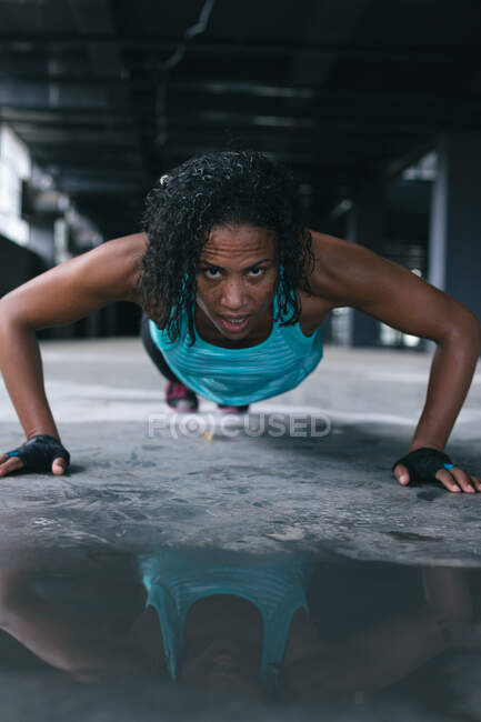 Femme afro-américaine portant des vêtements de sport faisant des pompes dans un bâtiment urbain vide. forme physique urbaine mode de vie sain. — Photo de stock