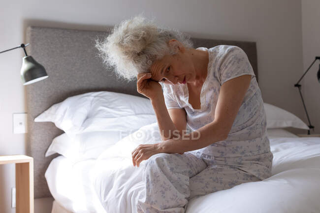 Старша жінка - козак почувається слабкою, сидячи на ліжку. Перебуваючи вдома в ізоляції під час карантину.. — стокове фото