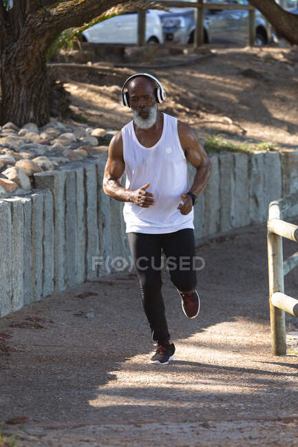 Sección media del hombre afroamericano mayor en forma haciendo ejercicio corriendo por el camino. retiro saludable estilo de vida fitness al aire libre. - foto de stock