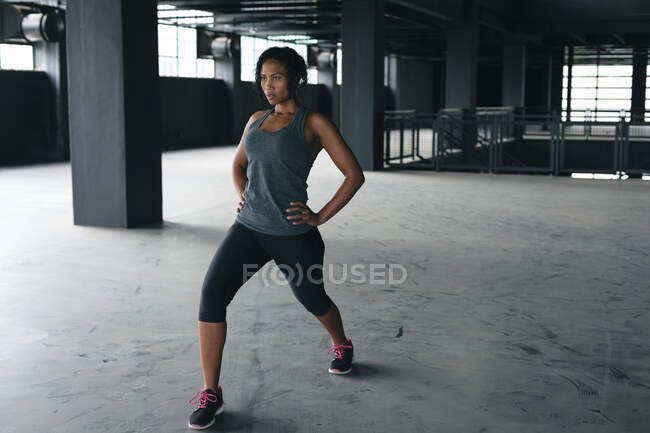 Mulher afro-americana de pé em um edifício urbano vazio e alongamento. fitness urbano estilo de vida saudável. — Fotografia de Stock