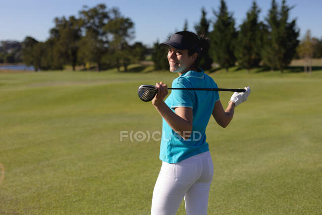 Белая женщина на поле для гольфа держит клюшку для гольфа за плечами, улыбаясь в камеру. спорт досуг хобби гольф здоровый образ жизни на открытом воздухе. — стоковое фото