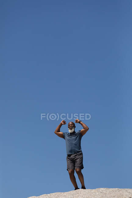 Fit älterer afrikanisch-amerikanischer Mann, der lächelnd die Fäuste in den blauen Himmel reckt. gesunder Lebensstil im Freien im Ruhestand. — Stockfoto