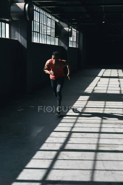 Homem afro-americano vestindo roupas esportivas correndo em prédio urbano vazio. fitness urbano estilo de vida saudável. — Fotografia de Stock