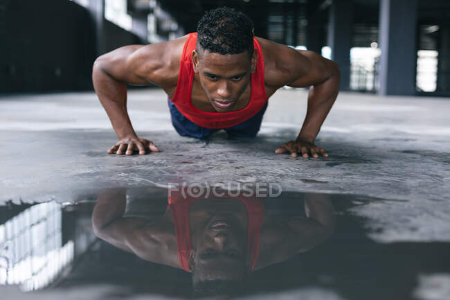 Un homme afro-américain portant des vêtements de sport faisant des pompes dans un bâtiment urbain vide. forme physique urbaine mode de vie sain. — Photo de stock