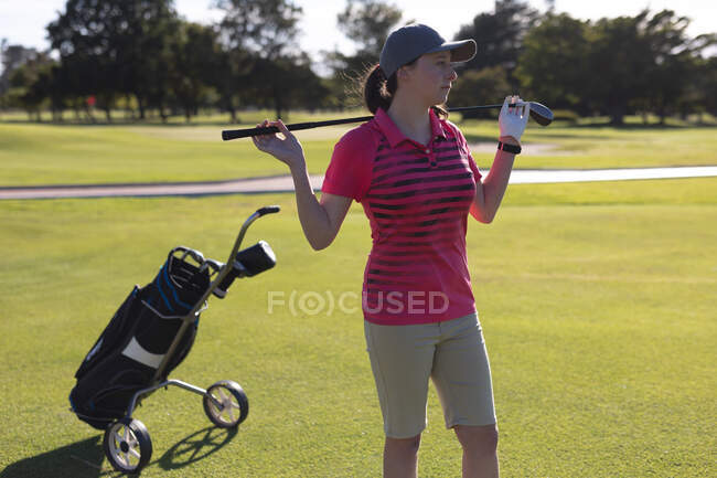 Mujer caucásica de pie en el campo de golf con acros club de golf hombros. deporte ocio aficiones golf estilo de vida al aire libre saludable. - foto de stock