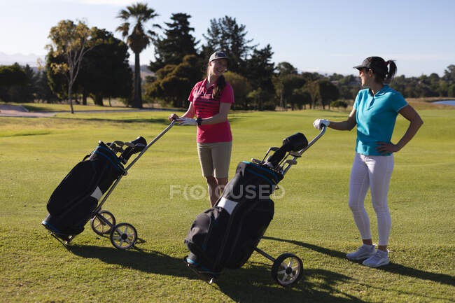 Two caucasian women on golf course holding golf bags and talking. sport leisure hobbies golf healthy outdoor lifestyle. — Stock Photo