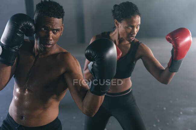African american man and woman wearing boxing gloves throwing punches in air in empty building. urban fitness healthy lifestyle. — Stock Photo