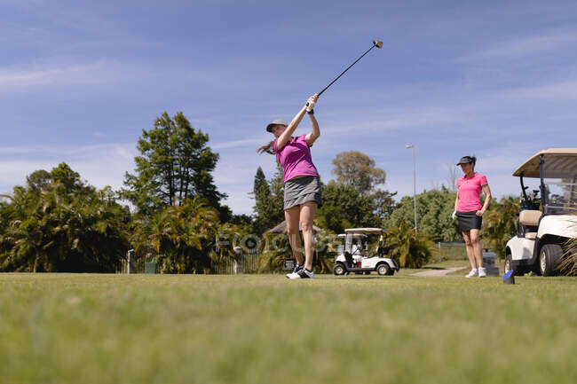 Duas mulheres caucasianas a jogar golfe, uma a baloiçar e a tentar. esporte lazer hobbies golfe saudável ao ar livre estilo de vida. — Fotografia de Stock