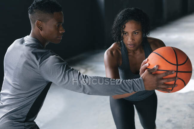 Africano americano homem e mulher de pé em um edifício urbano vazio e jogar basquete. fitness urbano estilo de vida saudável. — Fotografia de Stock