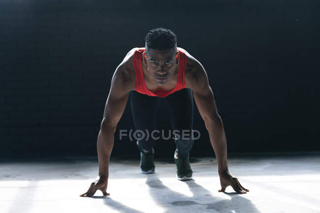 Afrikanischer Mann in Sportkleidung kniet in leerem städtischen Gebäude und beginnt zu rennen. urbane Fitness gesunder Lebensstil. — Stockfoto