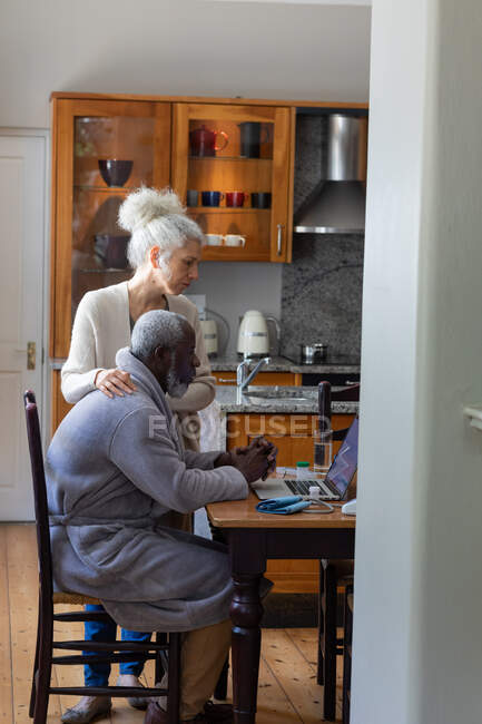 Couple mixte senior utilisant ordinateur portable payer des factures ensemble dans la salle à manger. rester à la maison en isolement personnel pendant le confinement en quarantaine. — Photo de stock