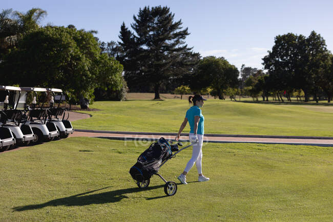 Mulher caucasiana atravessando campo de golfe puxando saco de golfe sobre rodas. esporte lazer hobbies golfe saudável ao ar livre estilo de vida. — Fotografia de Stock