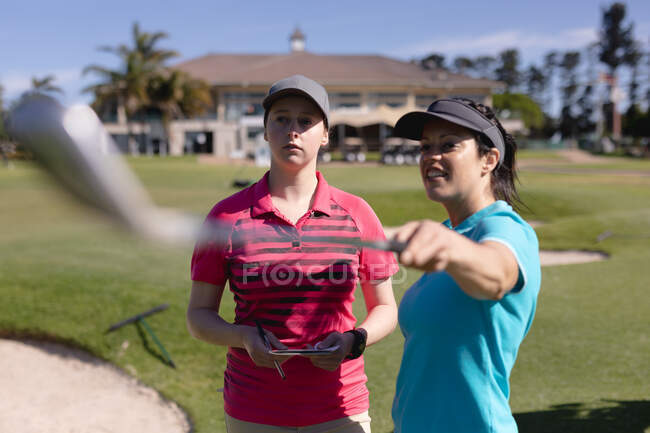Dos mujeres caucásicas jugando al golf hablando una apuntando con un palo de golf. deporte ocio aficiones golf estilo de vida al aire libre saludable. - foto de stock