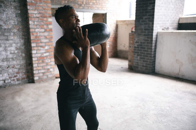 Homme afro-américain faisant de l'exercice avec un ballon de médecine dans un bâtiment urbain vide. forme physique urbaine mode de vie sain. — Photo de stock