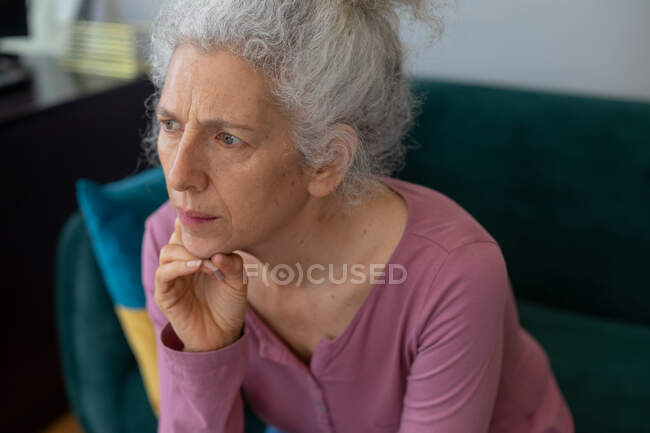Mulher caucasiana sênior sentada no sofá esfregando o queixo. ficar em casa em auto-isolamento durante o confinamento de quarentena. — Fotografia de Stock