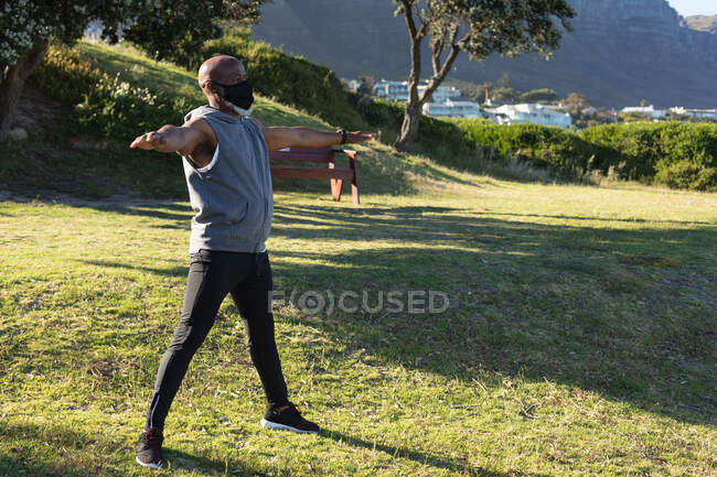 Fit senior african american man wearing face mask exercising outdoors stretching. healthy retirement outdoor fitness lifestyle hygiene during coronavirus covid 19 pandemic. — Stock Photo