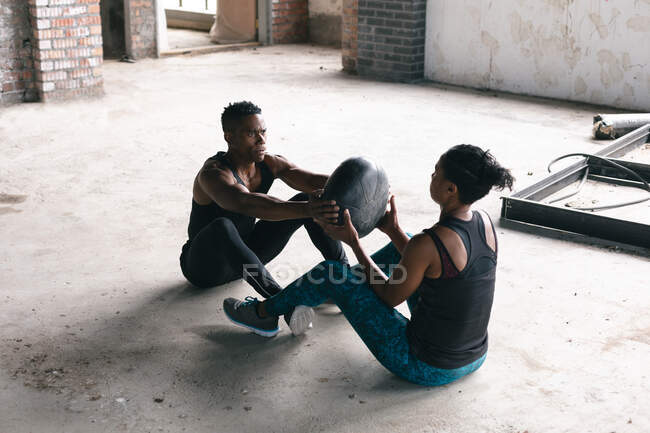 Homme et femme afro-américain faisant de l'exercice avec un ballon de médecine dans un bâtiment urbain vide. .urban fitness mode de vie sain. — Photo de stock