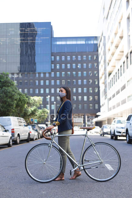 Африканська американка в масці на обличчі ходить з велосипедом на вулиці. Життя під час коронавірусної ковини 19. — стокове фото