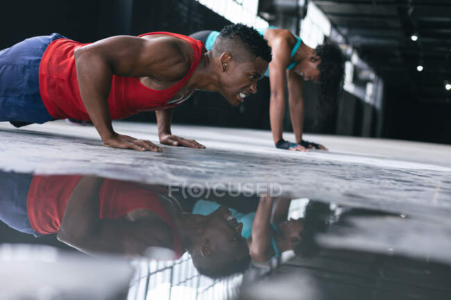 Afroamerikanische Männer und Frauen in Sportkleidung machen Liegestütze in einem leeren städtischen Gebäude. urbane Fitness gesunder Lebensstil. — Stockfoto