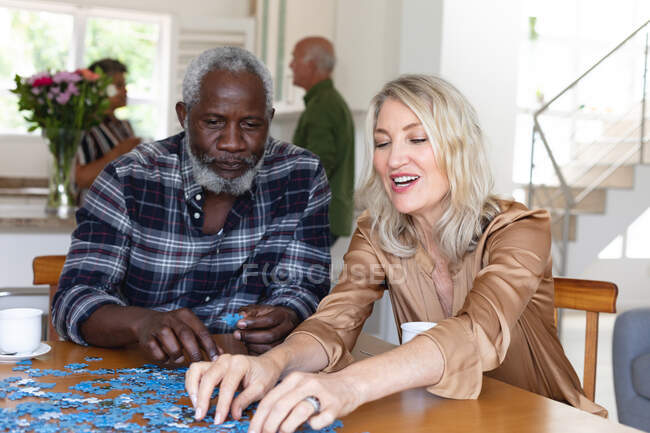 Senior caucasian woman and african american man sitting by table doing puzzles at home. senior retirement lifestyle friends socializing. — Stock Photo