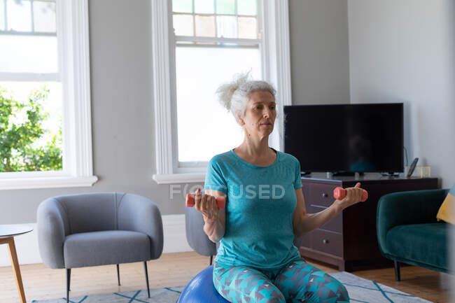 Eine ältere kaukasische Frau in Sportkleidung trainiert im Wohnzimmer. Während der Quarantäne zu Hause bleiben und sich selbst isolieren. — Stockfoto