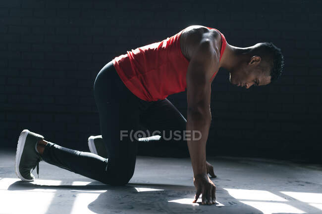 African american man wearing sports clothes kneeling starting to run in empty urban building. urban fitness healthy lifestyle. — Stock Photo