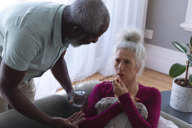 Femme caucasienne âgée couchée malade sur le canapé homme passant la médecine et l'eau dans le salon. rester à la maison en isolement personnel pendant le confinement en quarantaine. — Photo de stock