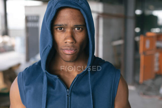 Portrait of african american man wearing hoodie looking at camera in empty urban building. urban fitness healthy lifestyle. — Stock Photo