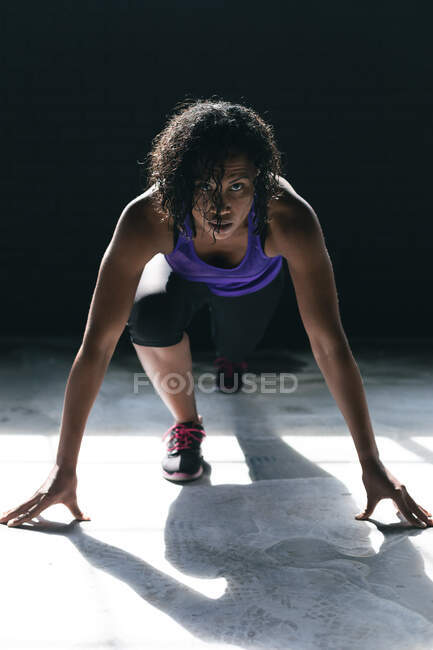 Eine Afroamerikanerin in Sportkleidung kniet in einem leeren städtischen Gebäude und rennt los. urbane Fitness gesunder Lebensstil. — Stockfoto
