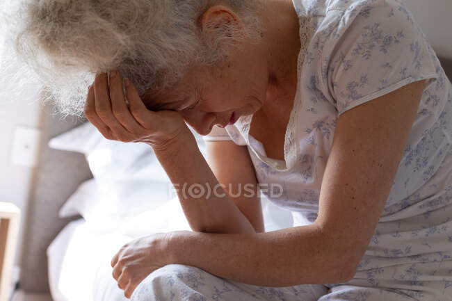 Donna caucasica anziana che si sente debole seduta sul letto. stare a casa in isolamento durante l'isolamento in quarantena. — Foto stock