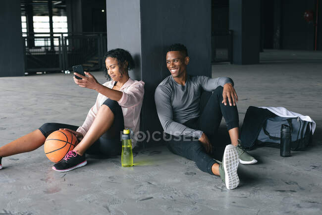 Homme et femme afro-américain assis dans un bâtiment urbain vide et se reposant après avoir joué au basket-ball. forme physique urbaine mode de vie sain. — Photo de stock