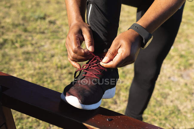 Low section of african american man exercising tying shoelaces. healthy retirement outdoor fitness lifestyle. — Stock Photo