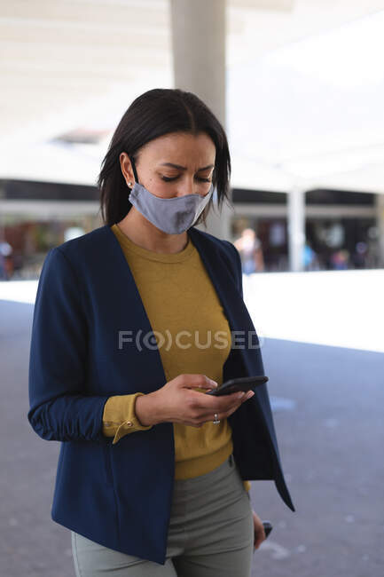 African american woman wearing face mask using smartphone on the street. lifestyle living during coronavirus covid 19 pandemic. — Stock Photo