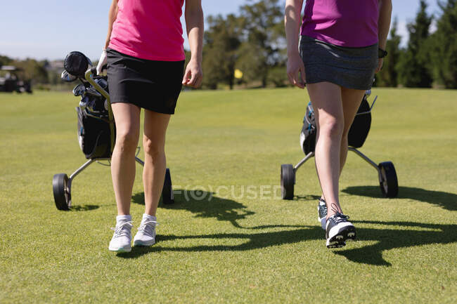 Низкая часть двух женщин, идущих по полю для гольфа, тянут сумки для гольфа на колесах. спорт досуг хобби гольф здоровый образ жизни на открытом воздухе. — стоковое фото