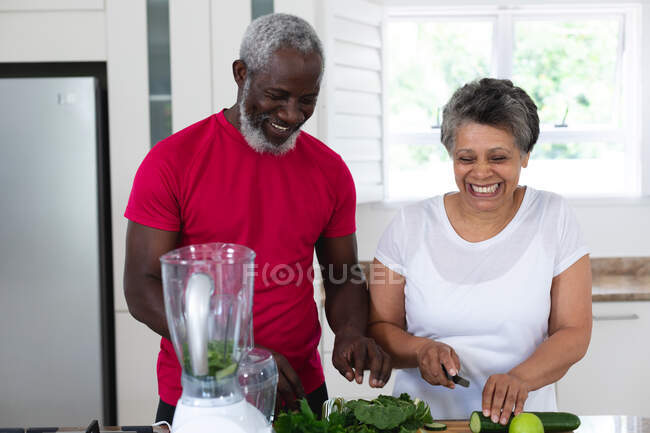 Senior african american man and woman preparing fruit and vegetable health drinks. health fitness wellbeing at senior care home. — Stock Photo