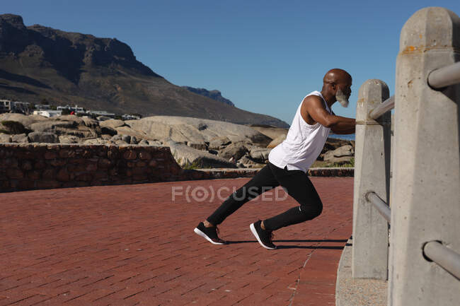 Ajuste o homem americano africano sênior que exercita-se inclinando-se no alongamento do fêmur. aposentadoria saudável ao ar livre fitness lifestyle. — Fotografia de Stock
